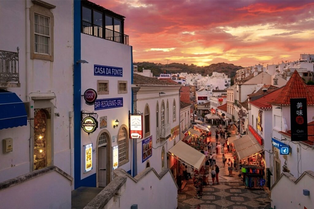 View of a lively pedestrian street in Albufeira Old Town at sunset, with restaurants, shops, and people enjoying the evening atmosphere