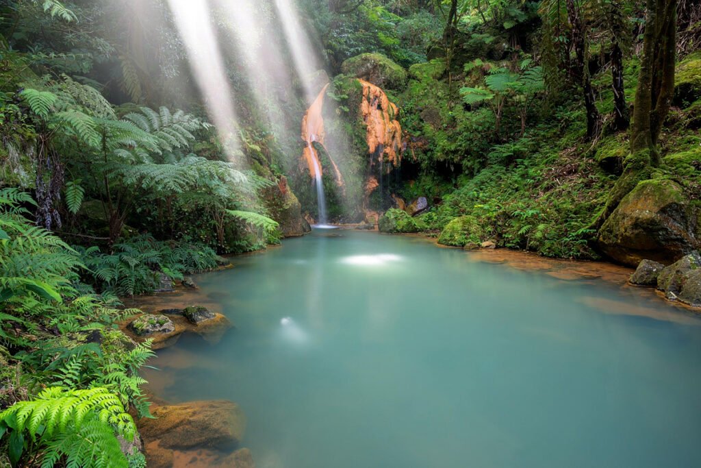 Natural thermal pool at Caldeira Velha, Sao Miguel, Azores. A waterfall flowing into a warm iron-rich basin surrounded by a lush tropical fern forest.
