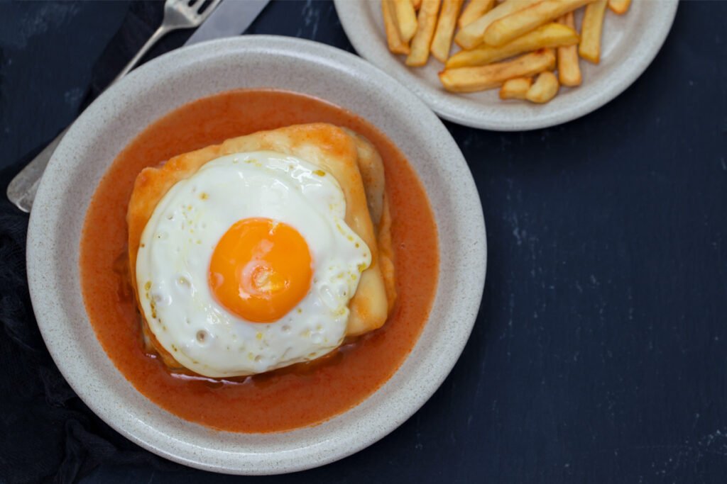 Francesinha, a traditional sandwich from Porto, layered with meats, melted cheese, and a thick spicy tomato and beer sauce, served with french fries