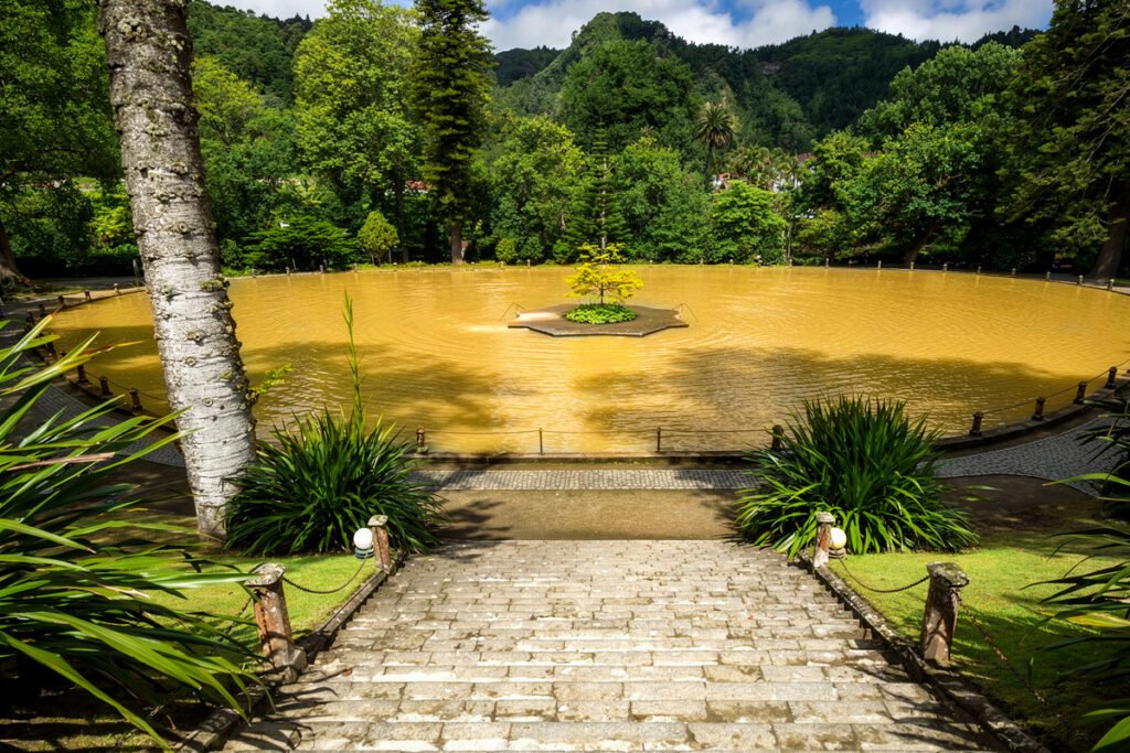 Large geothermal thermal pool with orange mineral-rich water at Terra Nostra Park, Azores