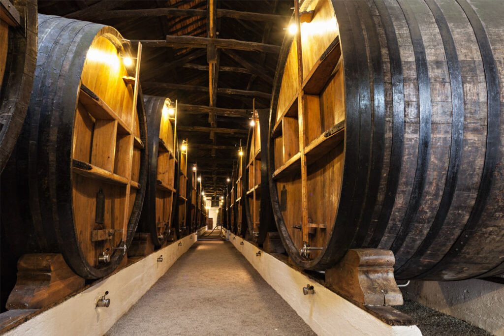 Interior view of a traditional Port Wine cellar in Vila Nova de Gaia, showing long rows of massive oak barrels aging wine in a dimly lit, historic warehouse