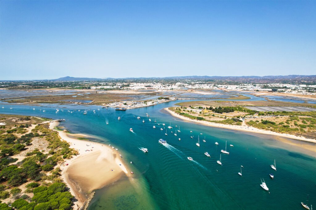 Aerial view of the Fuseta inlet in Ria Formosa Natural Park, showing turquoise water, boats, and sandy barrier islands in Algarve