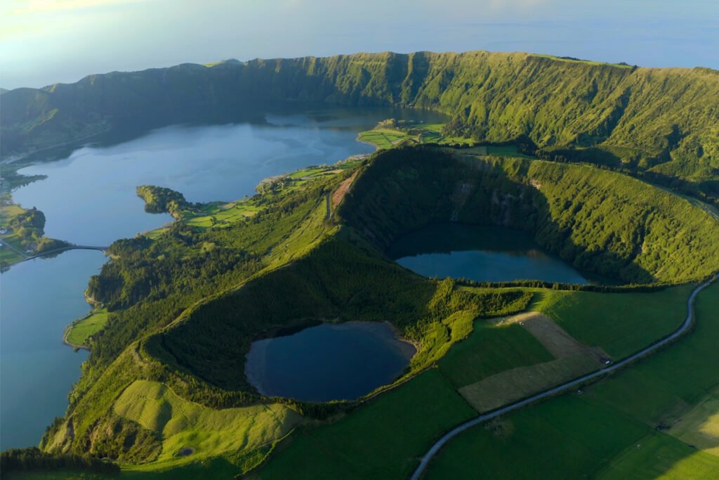 Perfect, let's keep it sharp and high-impact. Here are the direct versions in English for your São Miguel hero image: Alt Text (SEO - English) "Aerial view of Sete Cidades volcanic crater lakes in Sao Miguel, Azores, featuring Lagoa Azul and Lagoa de Santiago surrounded by lush green mountains
