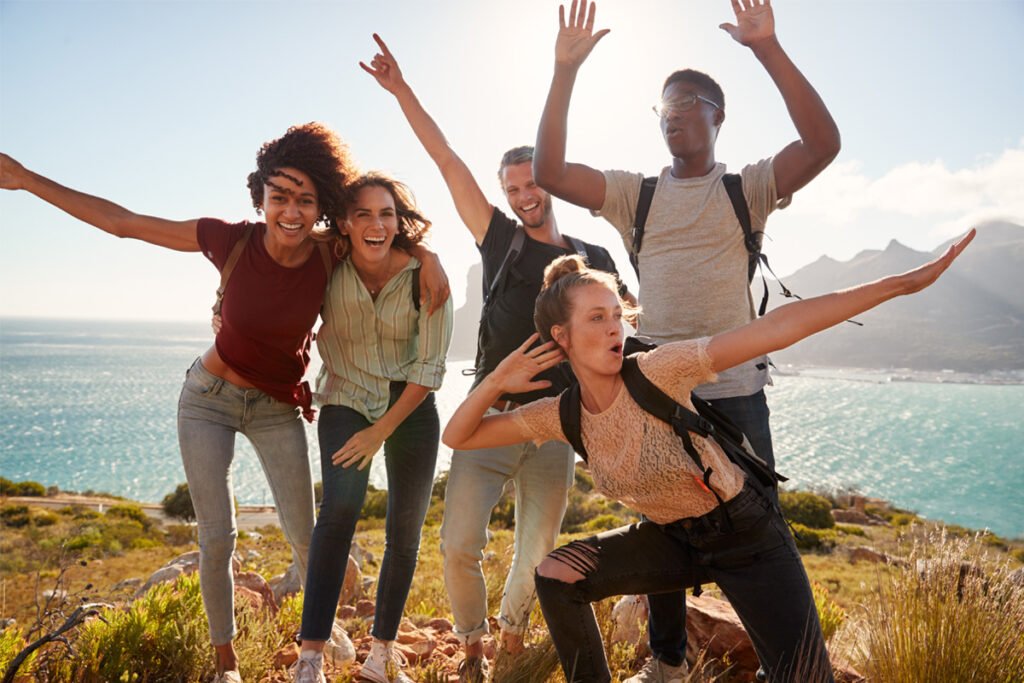A diverse group of happy travelers with backpacks celebrating on a mountain top overlooking the Atlantic coast of Portugal