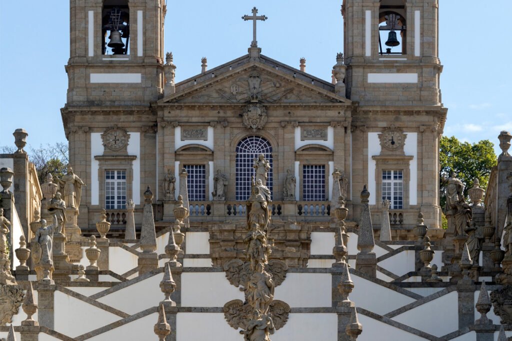 A stunning low-angle view of the ornate Baroque zig-zag stairway featuring numerous stone statues of saints leading up to the grand facade of the Bom Jesus Basilica in Braga, Portugal