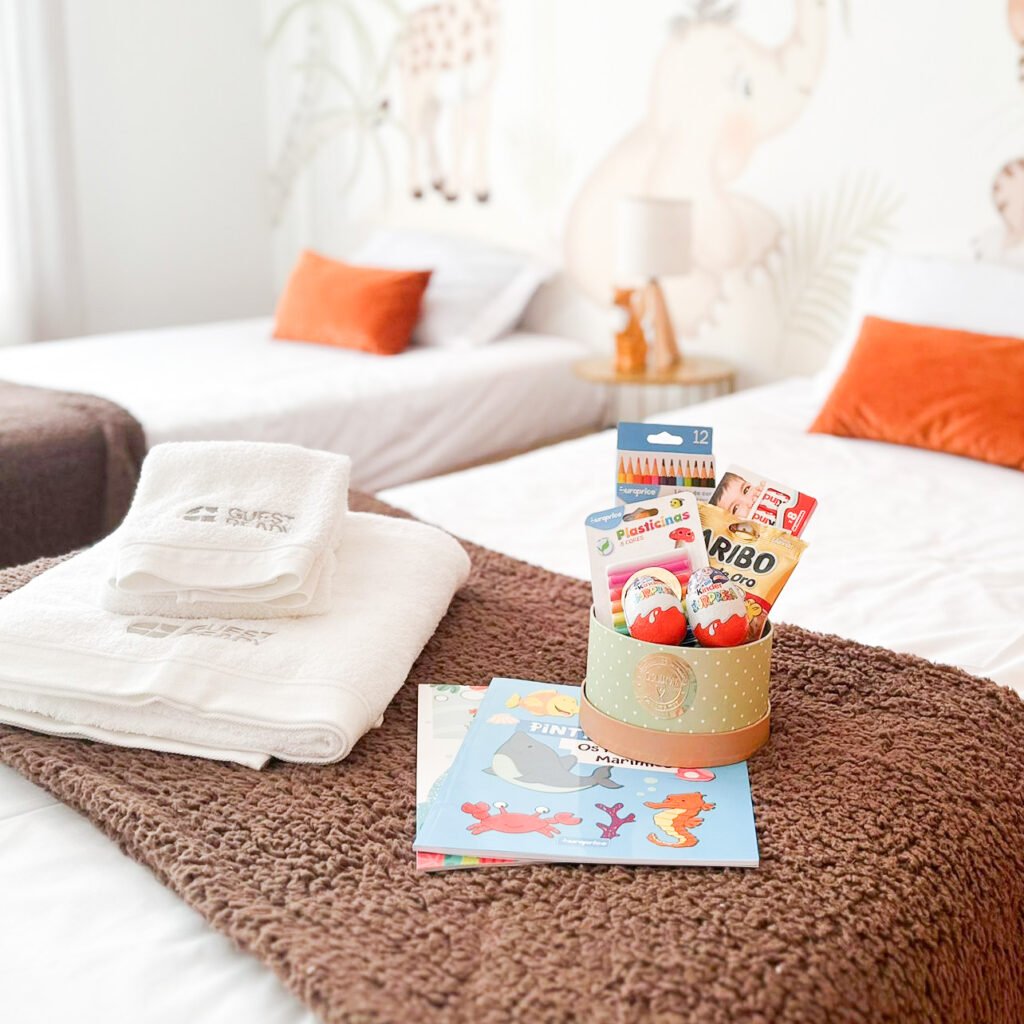 A detailed shot of a cozy kids twin bedroom in an oceanfront garden house in Madeira showing a personalized gift box filled with candies and coloring books on a blanket