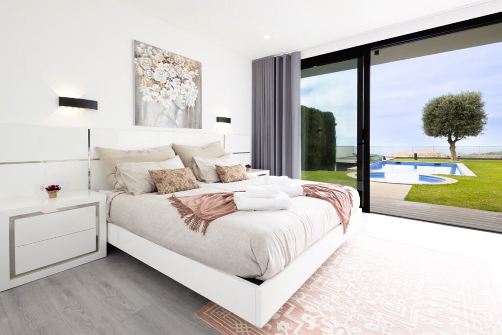 A stunning bright double bedroom with a sea view in an AL property in Caniço showcasing a cozy layout and massive sliding glass doors looking out directly onto the swimming pool and ocean