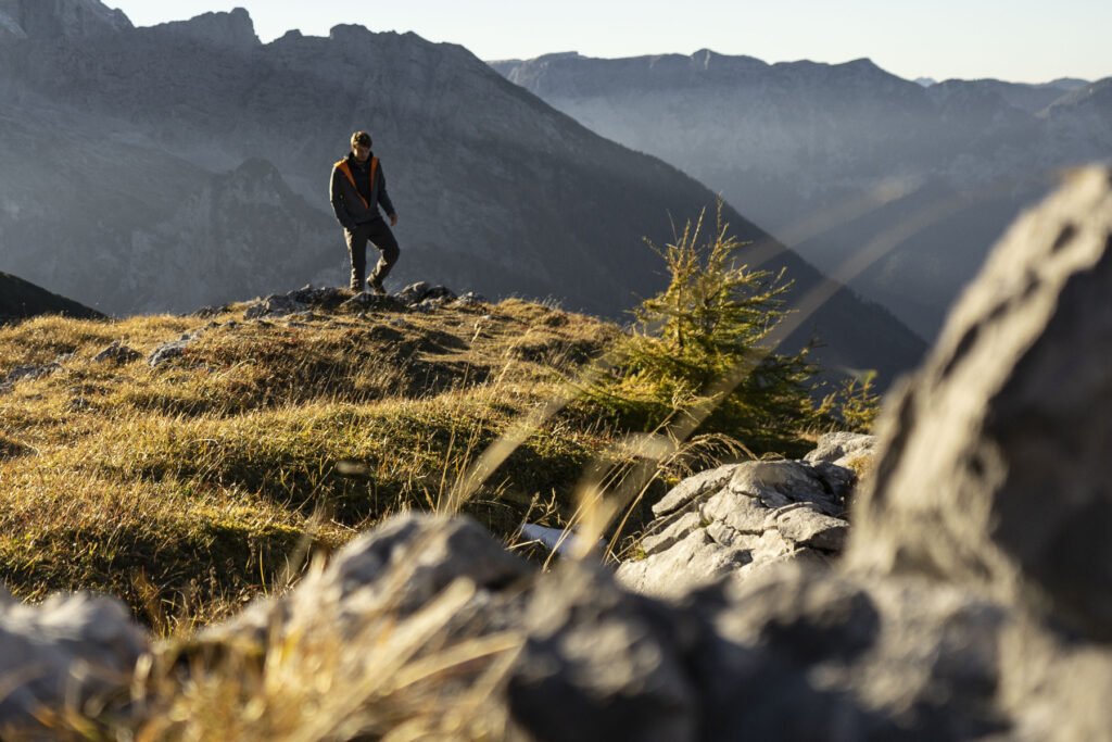 A hiker standing on a high mountain peak in Madeira Island overlooking dramatic ridges and valleys under bright sunlight
